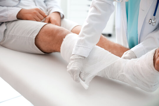 Doctor putting broken leg of young man in plaster