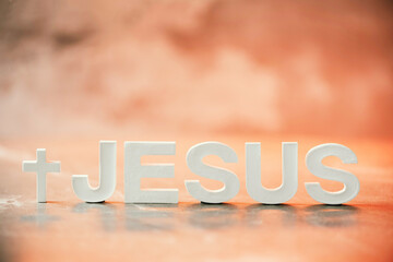 Name JESUS made with cement letters on orange light marble background. Copy space. Biblical, spiritual or christian reminder