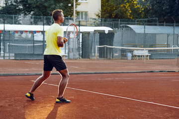 Young handsome man playing tennis on the tennis court