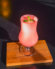 Pink fruit cocktail in a tall tulip glass served on a black wooden table in a restaurant.