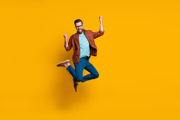 Fototapeta na wymiar Full length body size photo of male student jumping high gesturing like winner isolated on vibrant yellow color background