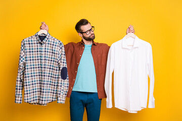 Photo portrait of bearded millennial choosing shirts in fitting room difficult decision isolated on...