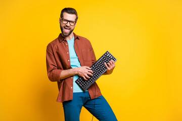 Photo portrait of bearded man keeping keyboard playing like guitar isolated on bright yellow color...