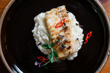 Fish fillet baked with rice on a black plate close-up.