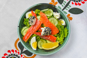 Close up of smoked salmon salad with boiled eggs, cucumbers, cream cheese with sesame seeds and a piece of lemon.