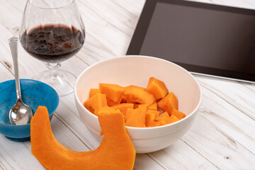 Ingredients for pie. Pumpkin pieces, raisin in cognac, little turquoise bowl, touchpad near. Concept of cooking with internet recipe. Web learning of food preparing. White wooden table.