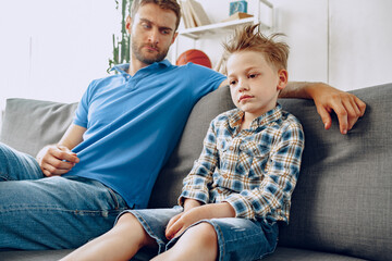 Father is having a talk with his little son while sitting on couch at home
