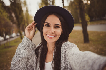 Photo portrait of happy brunette in black hat taking selfie outside smiling wearing grey clothes