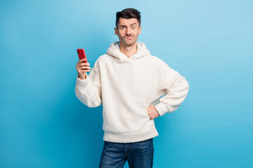 Photo portrait of unhappy waiting man holding phone in one hand wearing woolen hoodie isolated on...