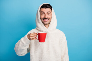 Photo portrait of smiling man holding red coffee cup wearing woolen hoodie isolated on pastel blue...