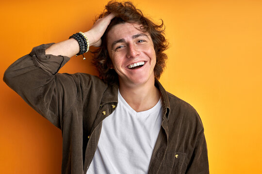 portrait of happy curly young man isolated over orange studio background, handsome guy shine with happiness, has perfect toothy smile