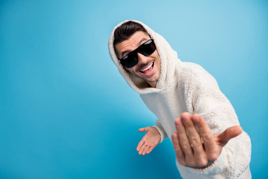 Photo portrait of cool guy in black glasses telling you to come here showing blank space wearing wool hoodie isolated on pastel blue colored background