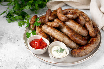 Fried sausages. Bavarian and Nuremberg sausages with spices, sauce, tomatoes and parsley. Delicious meat sausages in a white ceramic plate on a light gray table. German dish