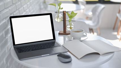 Laptop with a notebook and coffee on a white table in a modern cafe.