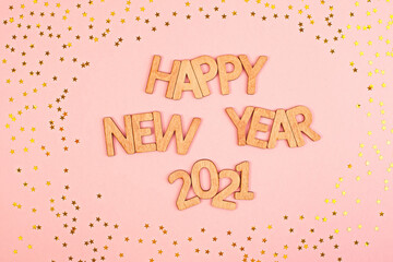 Cheerful wooden lettering happy new year 2021 on a soft pink background with gold stars.