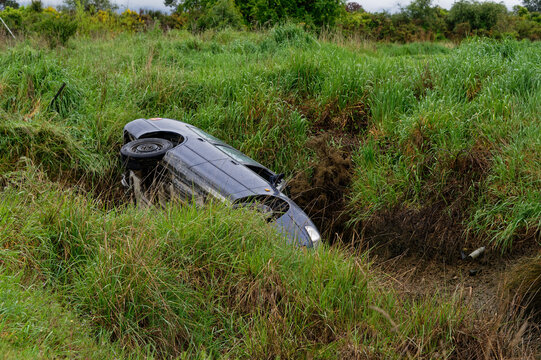 A Car Has Run Off The Road, Over A Bank And Is Lying On Its Side