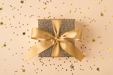 Top above overhead close up view photo of beautiful present box with golden yellow ribbon on background with shiny confetti soft beige color