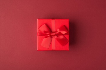 Flat lay layout close up view photo of small present box with bow and ribbon isolated maroon color background