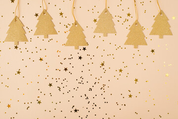 Merry Christmas composition concept. Close up view flatlay photo of cute trees label on string on shiny confetti golden beige color soft pastel backdrop with blank empty space