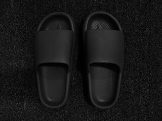 Monotone color of pairs of black rubber slipper for indoor on black carpet background.