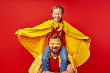 kid girl on dad's neck, play superhero game, imitate flight, smile. happy parent and daughter in supehero costumes posing at camera, smile