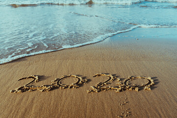 Goodbye 2020 lettering on sunset beach with wave and sea. Handwritten inscription 2020 on beautiful golden sand beach.