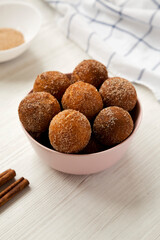 Homemade Fried Donut Holes in a pink bowl on a white wooden background, side view.