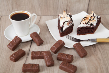 Delicious chocolate candies with cake and coffee on a wooden background.