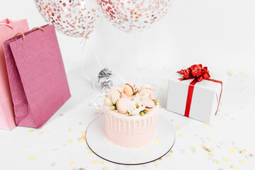 White beautiful cake, decorated with flowers, boxes with gifts, for birthday, on a white background with balloons