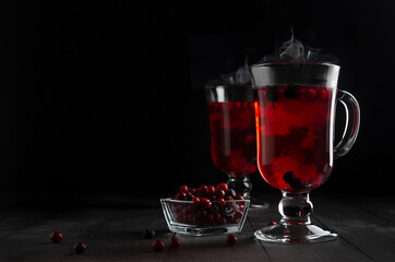 Christmas bright red mulled wine with berries, steam, ripe cowberry, blueberry in two glass wine glasses on black wood table in dark interior, copy space..