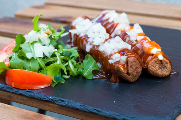 American junk food in a simple composition. crispy Fried sausages or hot dog with mayo and ketchup sauce and chopped onion. Some vegetables around like salad and tomatoes on a wooden background