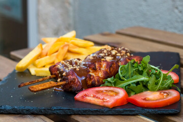 American fast food. A couple of beef and chicken skewers with a delicious peanuts sauce with some fresh salad with tomatoes and crunchy french fries. Delicious meat steaks on a wooden background