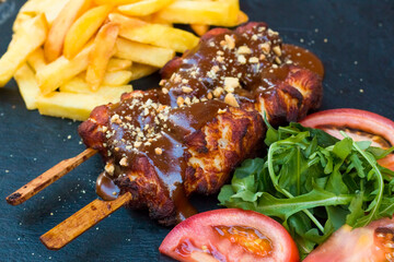 American fast food. A couple of beef and chicken skewers with a delicious peanuts sauce with some fresh salad with tomatoes and crunchy french fries. Delicious meat steaks on a wooden background