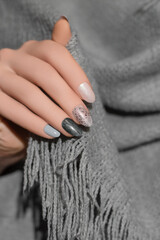 Female hand with glitter gray nail design. Silver nail polish manicure. Woman hand hold grey wool...