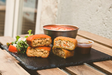 Classic, Italian arancini. deep fried Rice balls with minced meat and some vegetables inside. Tasty crunchy food with peanuts sauce and tomatoes soup with mozzarella cheese on the top. Close up view