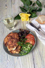 Schnitzel from chicken breast, vegetables and a glass of wine on a wooden table close-up