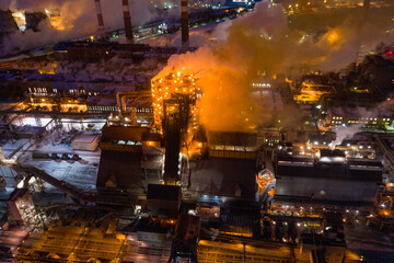 Aerial view of steel plant at night with smokestacks and fire blazing out of the pipe. Industrial panoramic landmark with blast furnance of metallurgical production. Concept of environmental pollution