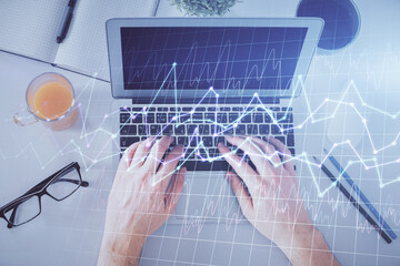 Double exposure of man's hands typing over laptop keyboard and forex chart hologram drawing. Top view. Financial markets concept.