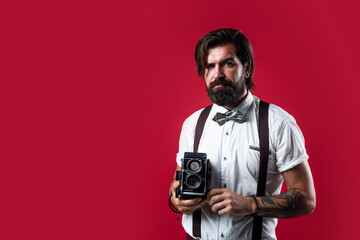 mature serious man in suspenders using retro camera over red background, photographing