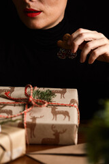 Girl with red lips holds a gingerbread man cookie with chocolate and anise, with her left hand. Surrounded by Christmas presents