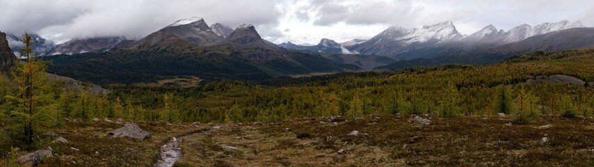 A panorama of a hiking trail surrounded by mountains during rain with snow in the backcountry of...
