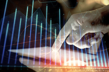 Double exposure of man's hands holding and using a digital device and forex graph drawing. Financial market concept.