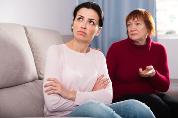 Sad mature female and daughter sitting at sofa after quarrel at home
