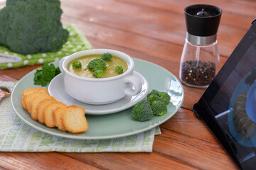 Broccoli. Homemade cream soup of broccoli with croutons following a recipe on tablet.  Healthy eating without calories but with vitamins. Concept of healthy nutrition. Wooden background