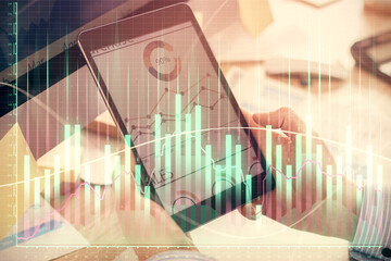 Double exposure of man's hands holding and using a phone and financial graph drawing. Analysis concept.