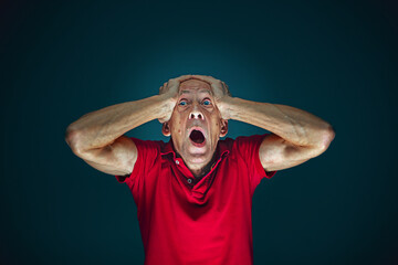 Head in hands. Portrait of crazy scared and shocked caucasian man isolated on dark background....