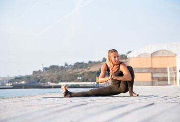 middle-aged female doing sitting yoga asana on one leg on the sunny beach at