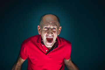 Fototapeta premium Screaming. Portrait of crazy scared and shocked caucasian man isolated on dark background. Copyspace for ad. Bright facial expression, human emotions concept. Watching horror on TV, cinema.
