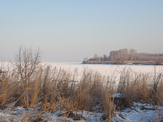 Riverbank with trees. Grass. The river is under the ice. Winter day. Russian winter nature. Russia, Ural, Perm Region