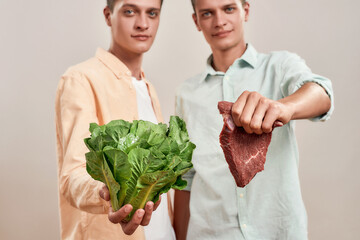 Choosing healthy eating. Two young caucasian twin brothers holding fresh green salad and piece of...